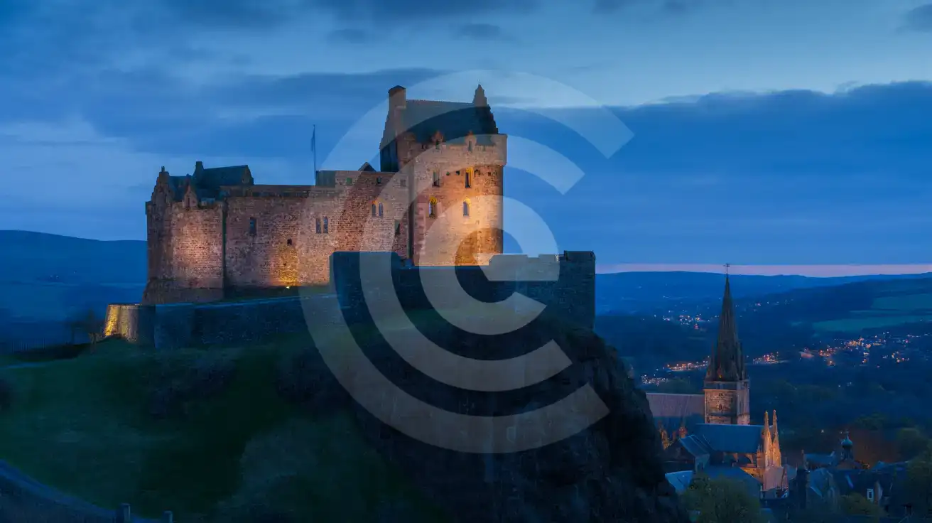 Le château d'Édimbourg illuminé par des projecteurs à l'heure bleue, avec les lumières de la ville scintillant en dessous
