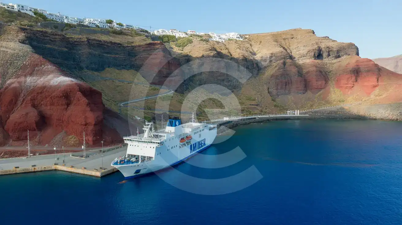 Aerial view of a ferry docked at Santorini's volcanic port with the switchback road climbing toward the clifftop villages