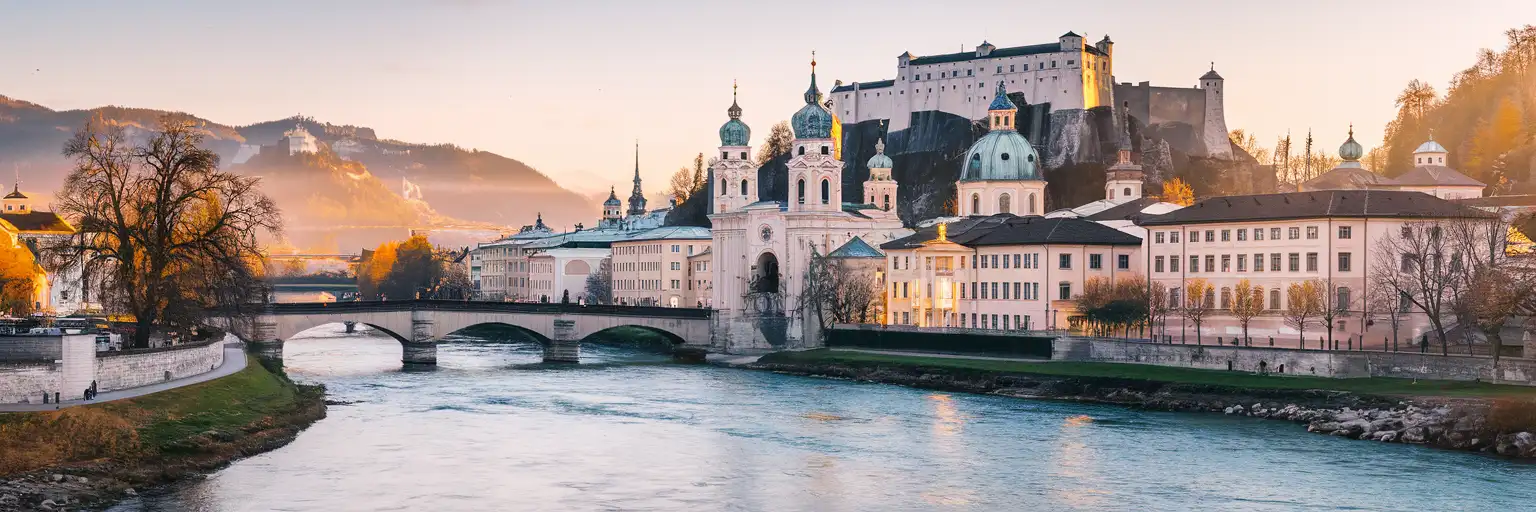 Hohensalzburg Fortress rising above the Salzach River and Salzburg Old Town at golden hour with the Austrian Alps in the background