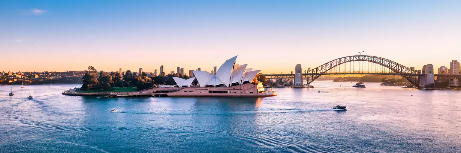 Sydney Opera House and Harbour Bridge at golden hour with boats on Sydney Harbour