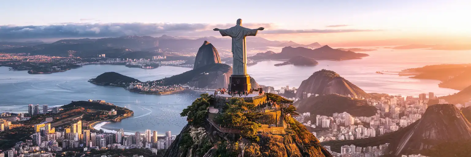 Christ the Redeemer statue atop Corcovado Mountain overlooking Rio de Janeiro at golden hour with Sugarloaf Mountain and Guanabara Bay in the background