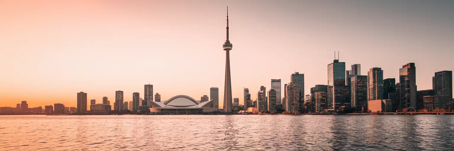 CN Tower rising above the Toronto skyline at golden hour with Lake Ontario harbor waters in the foreground