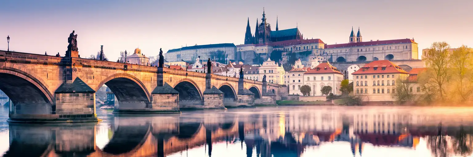 Charles Bridge and Prague Castle at golden hour with the Vltava River and historic Old Town rooftops in Czech Republic