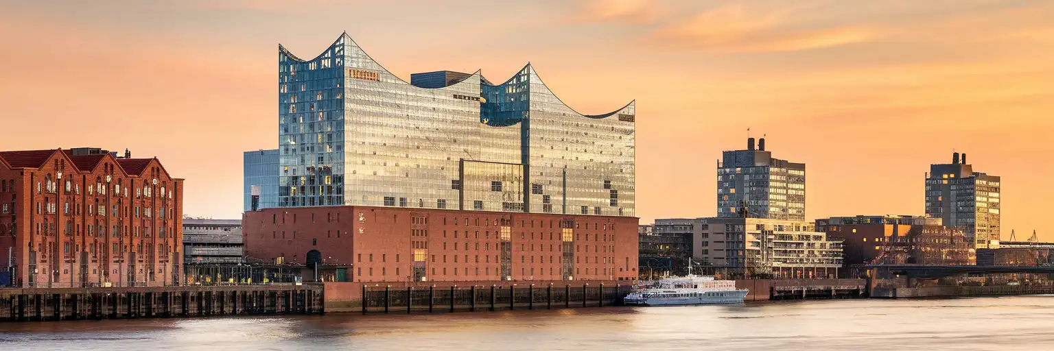 The Elbphilharmonie concert hall rising above Hamburg's HafenCity waterfront at golden hour with the Elbe River in the foreground