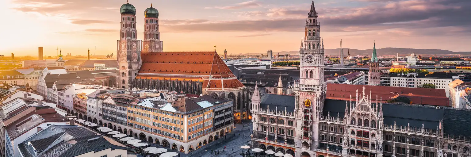 Munich Frauenkirche twin towers and Marienplatz at golden hour with Bavarian Alps in the distance