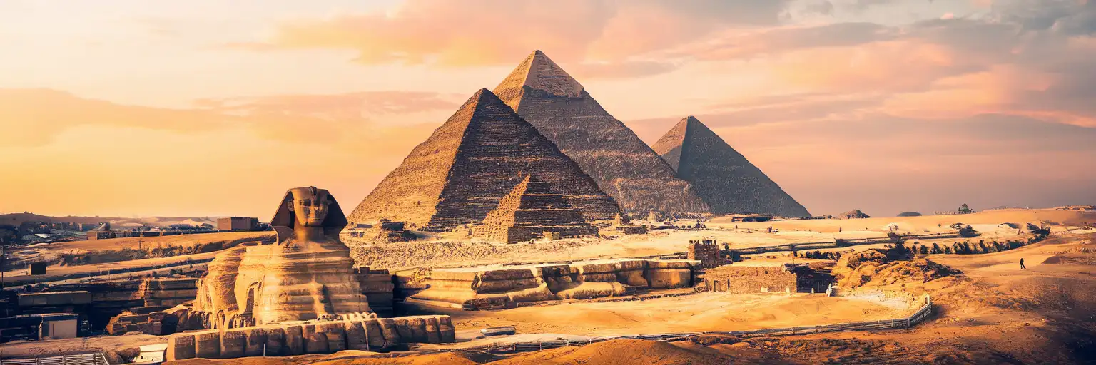 The Great Pyramid of Giza and Sphinx at golden hour with Cairo skyline in the distance