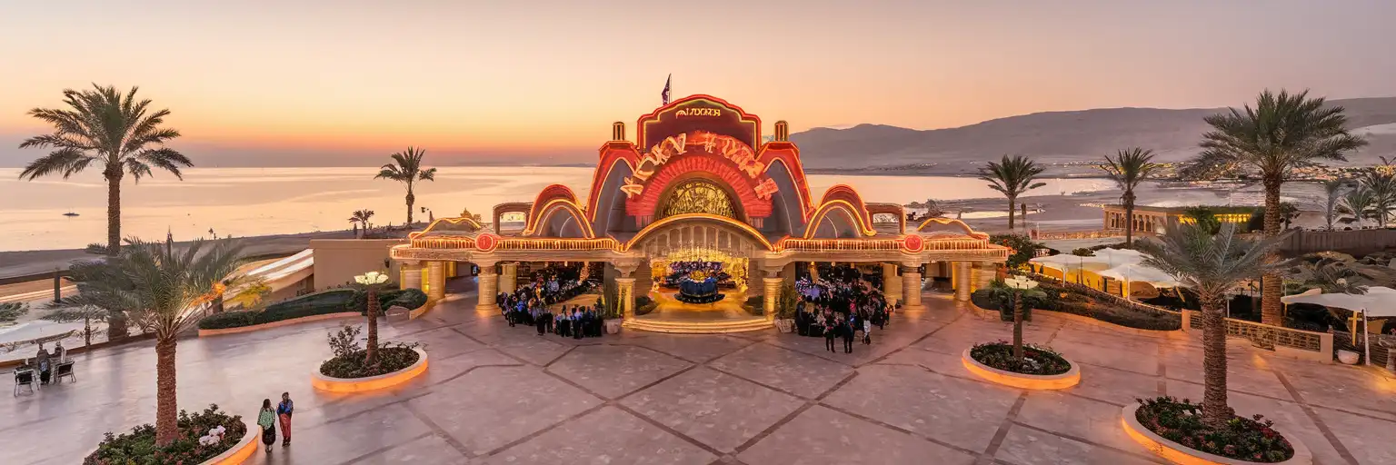 Neon-lit entrance of Hollywood Sharm El Sheikh entertainment district at golden hour with palm trees and Red Sea mountains in background