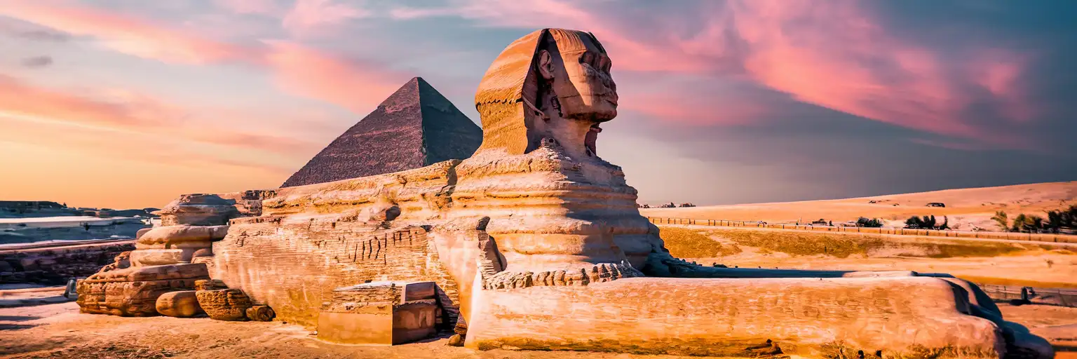 The Great Sphinx of Giza in profile at golden hour with the Pyramid of Khafre rising behind it against a warm desert sky