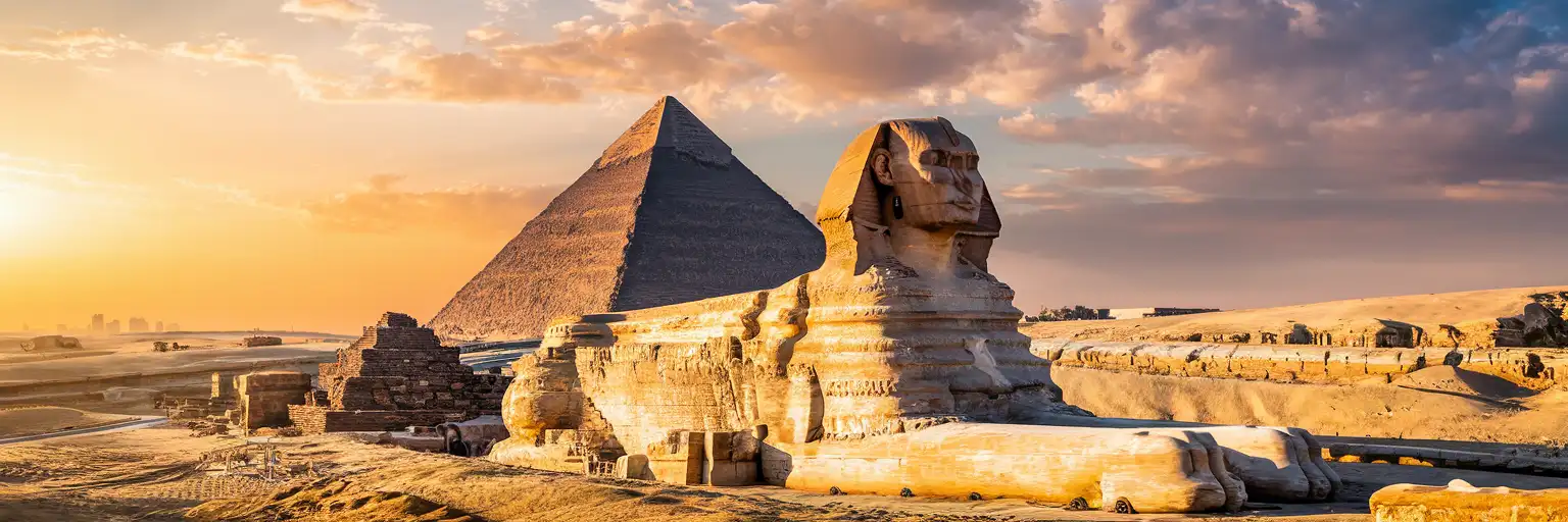 The Great Pyramid of Giza and the Great Sphinx at golden hour with the desert expanse and distant Cairo skyline
