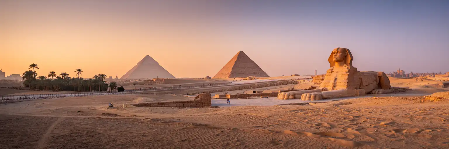 A Grande Pirâmide de Gizé e a Esfinge ao pôr do sol com o horizonte do Cairo ao fundo