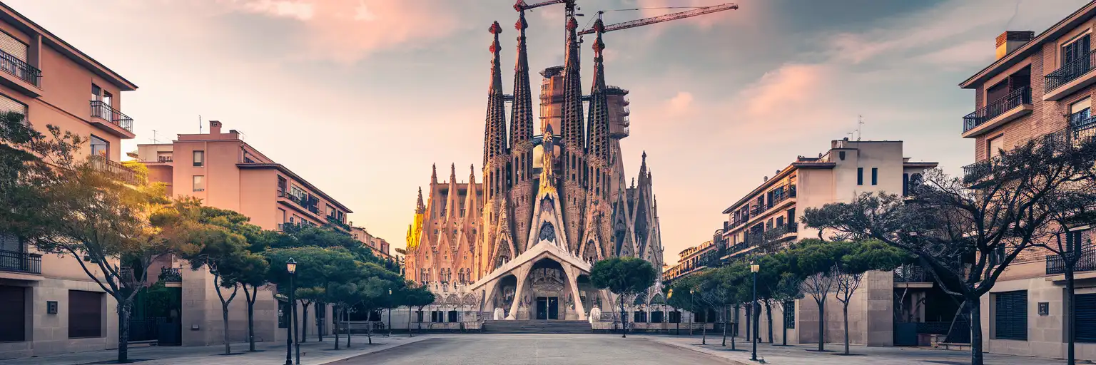 Wide golden-hour view of the Sagrada Família in Barcelona with the surrounding city blocks