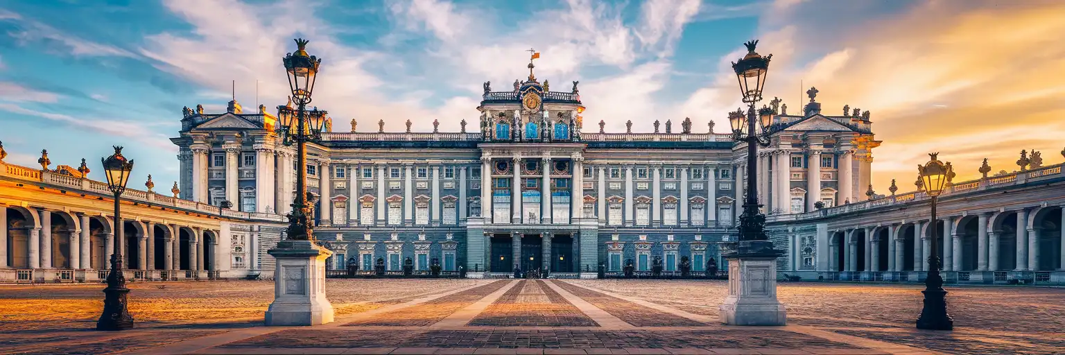 The grand white limestone facade of the Royal Palace of Madrid at golden hour with Plaza de la Armería in the foreground