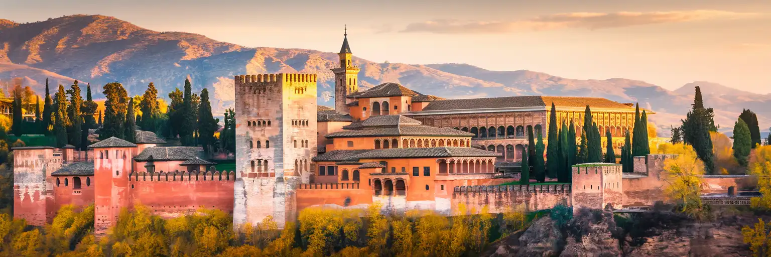 The Alhambra palace complex at golden hour with the Alcazaba towers and Sierra Nevada mountains in Granada, Spain
