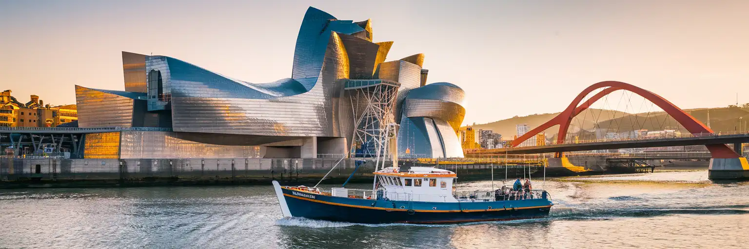 Panoramic view of Bilbao's Nervión River with traditional trainera boats and the Guggenheim Museum's titanium architecture at golden hour