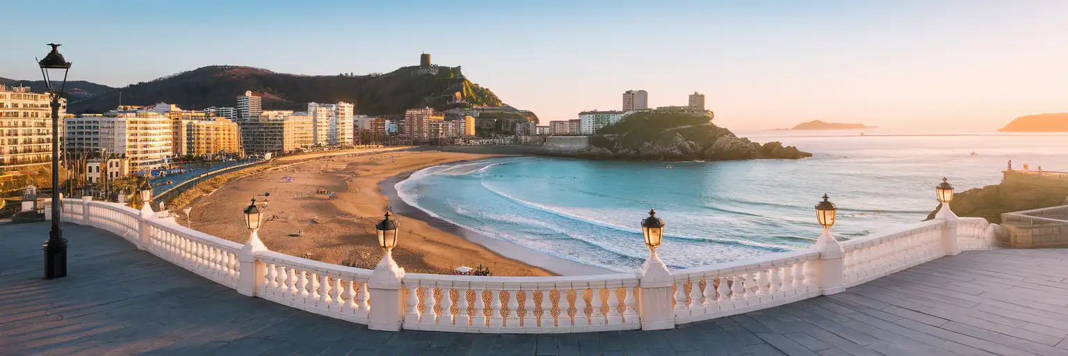 La Concha Bay in San Sebastian at golden hour with the crescent beach, white promenade railings, and Monte Urgull in the background