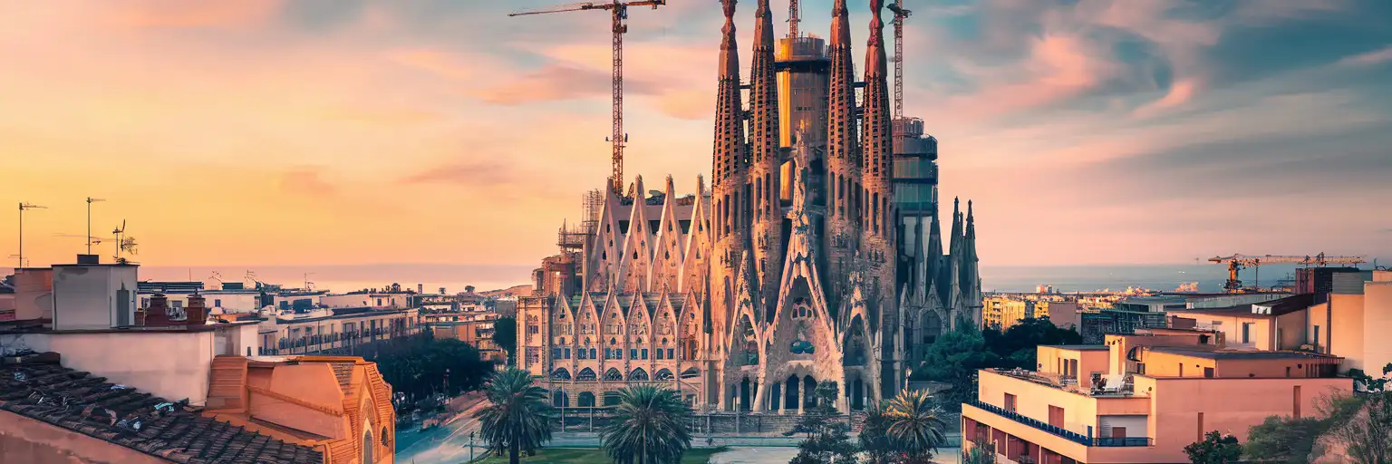 Sagrada Família cathedral in Barcelona at golden hour with its ornate spires rising above the Eixample neighborhood and Mediterranean Sea in the distance