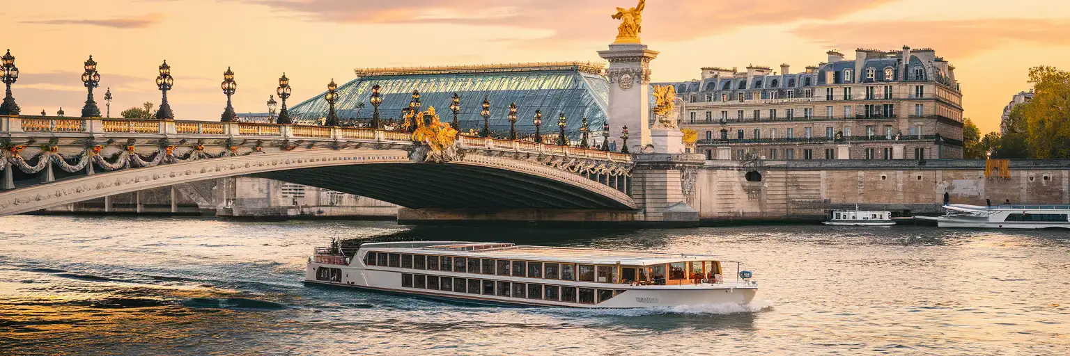 Seine River cruise boat passing under Pont Alexandre III bridge at golden hour in Paris