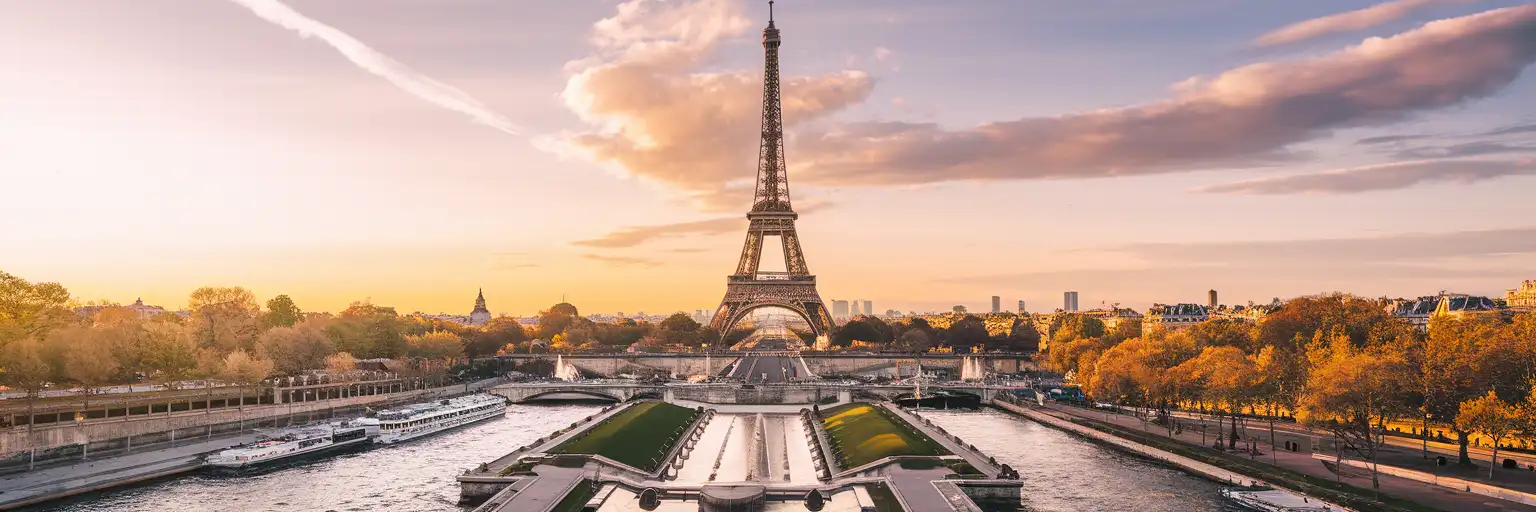 Eiffel Tower rising above the Champ de Mars gardens at golden hour with the Seine River and Parisian rooftops in the distance