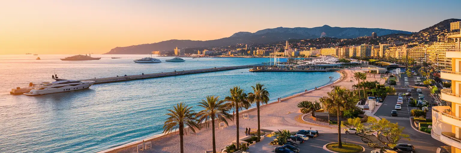 Boulevard de la Croisette waterfront promenade in Cannes at golden hour with palm trees, Mediterranean Sea, and luxury hotels