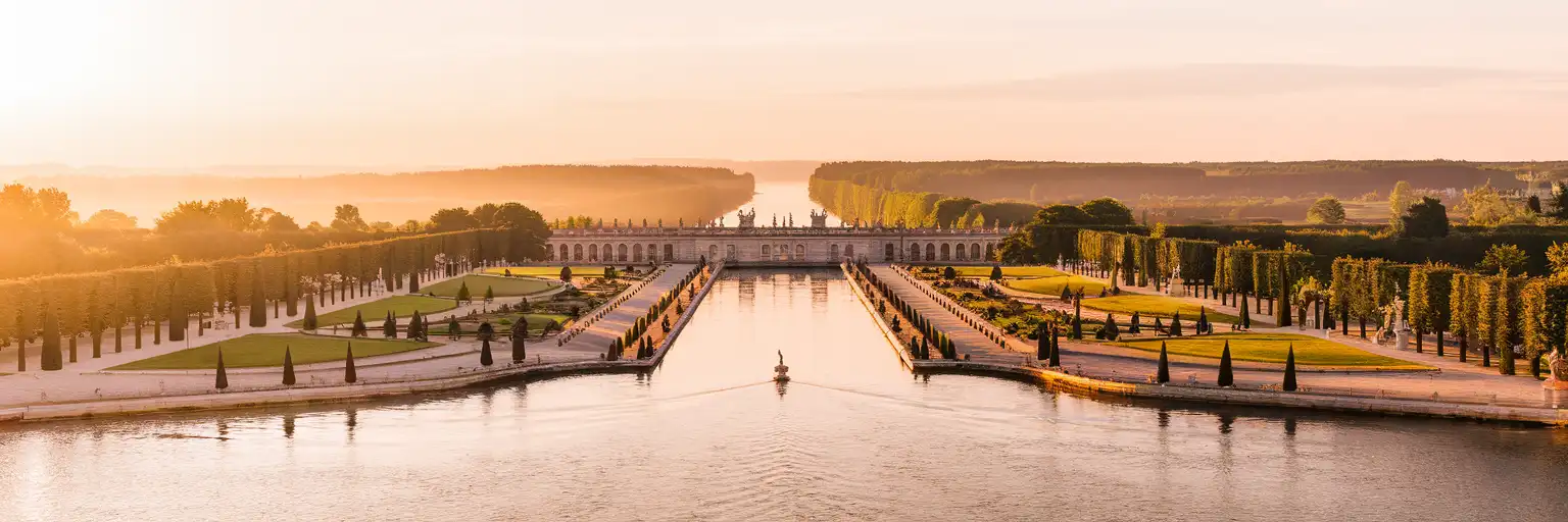The Grand Canal at Versailles stretching toward the horizon at golden hour with formal French gardens on either side