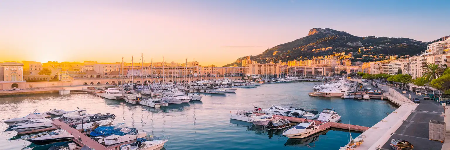 Wide exterior view of Port of Nice at golden hour with marina, harborfront buildings, and cruise berths