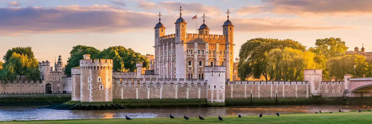 The Tower of London's White Tower and medieval fortifications glowing at golden hour with Tower Bridge visible along the Thames