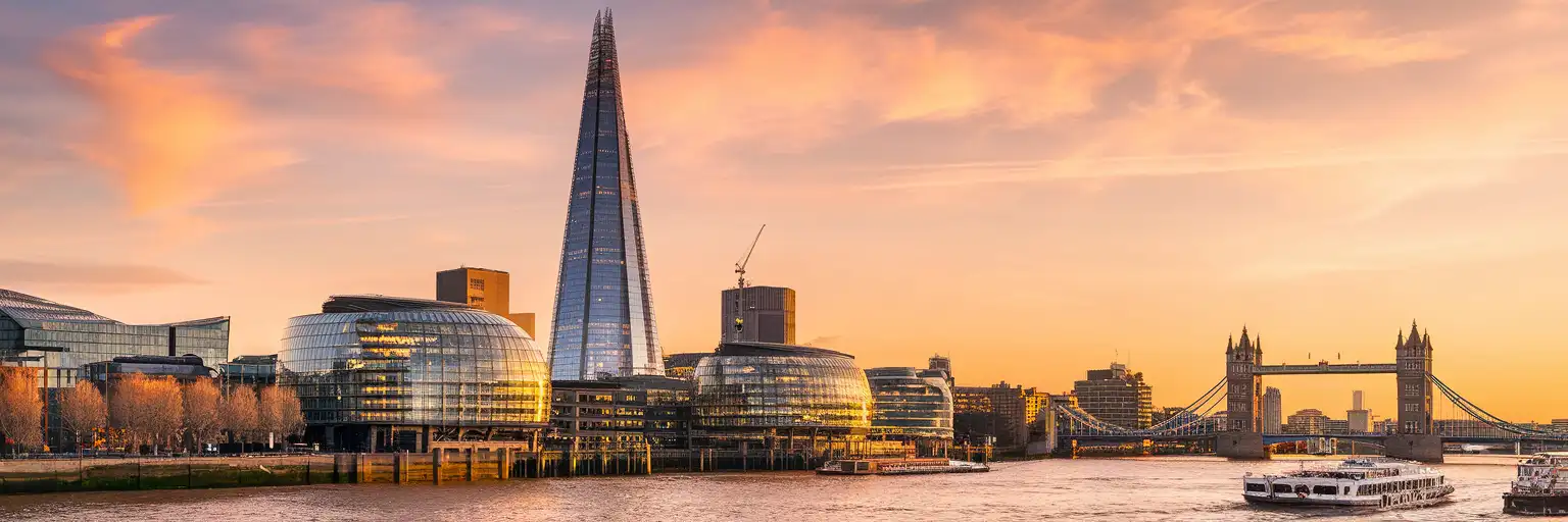 The Shard skyscraper rising above the London skyline at golden hour, viewed from the Thames south bank with Tower Bridge in the distance