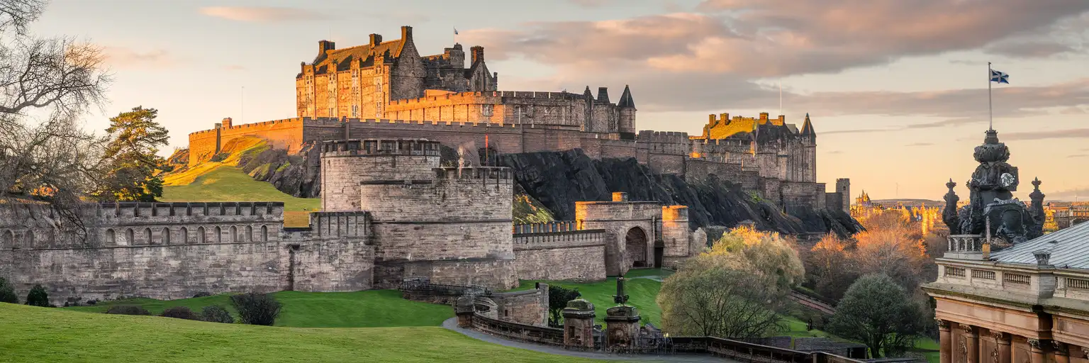 Edinburgh Castle rising dramatically above Castle Rock at golden hour, viewed from Princes Street Gardens with the Scottish flag flying
