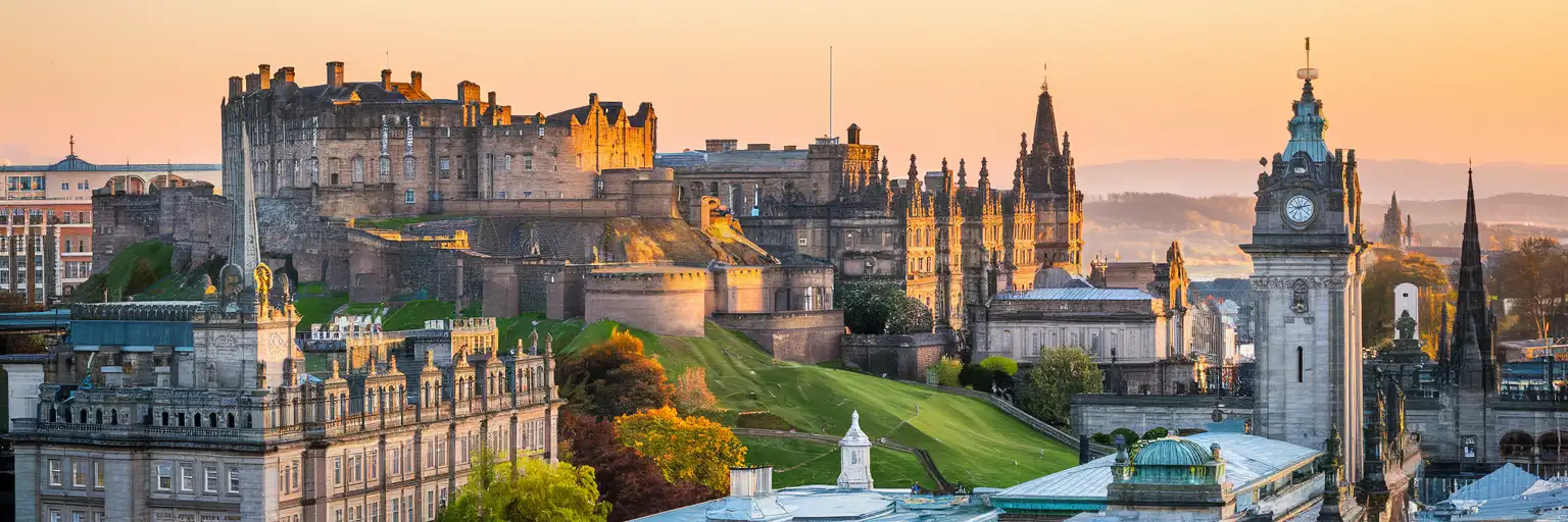 Edinburgh Castle illuminated by golden-hour sunlight atop Castle Rock with the Old Town rooftops and Princes Street Gardens stretching below