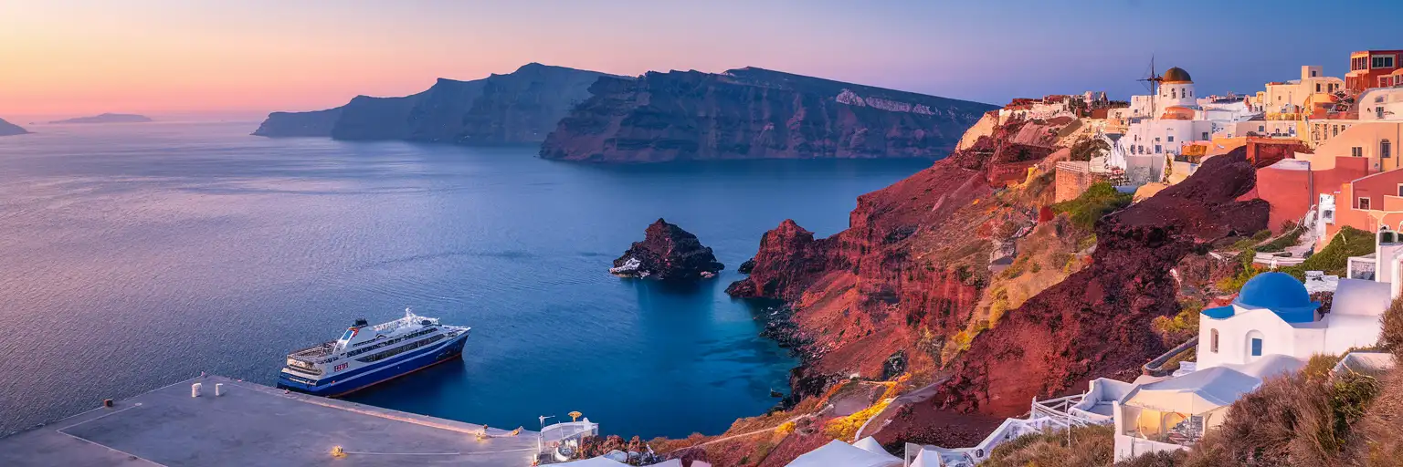 Athinios ferry port at Santorini carved into volcanic caldera cliffs with ferry docked and Fira visible on the rim above at golden hour