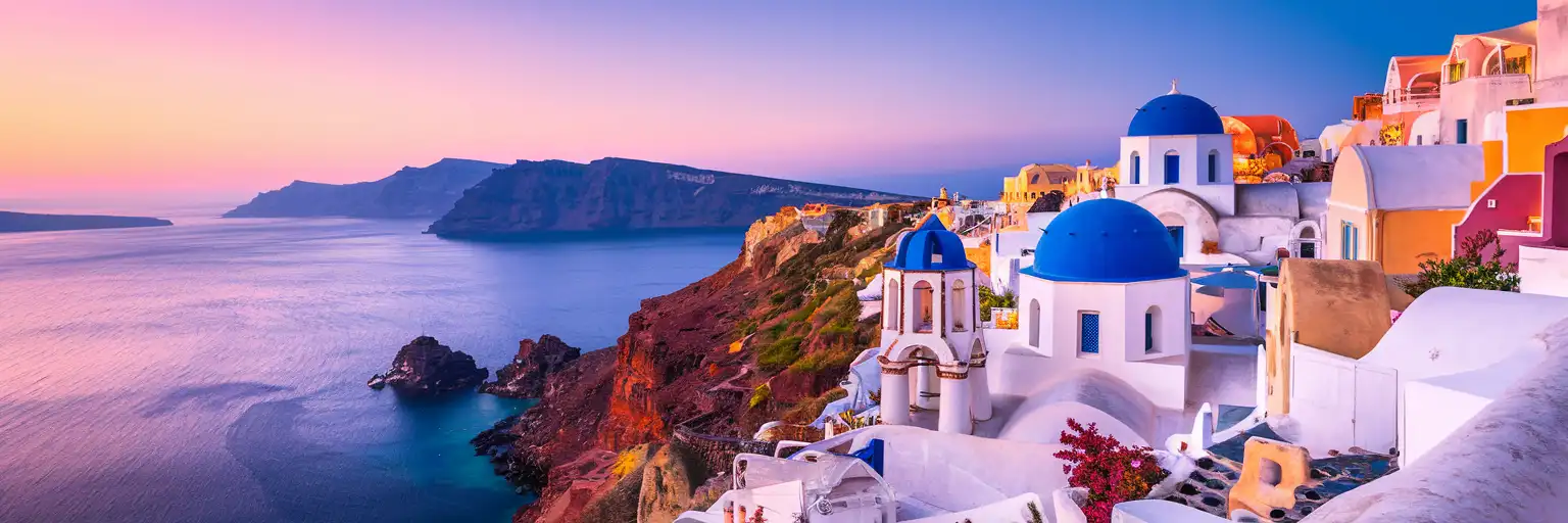 White-washed buildings and blue-domed churches of Oia village cascading down Santorini's volcanic caldera cliffs at golden hour