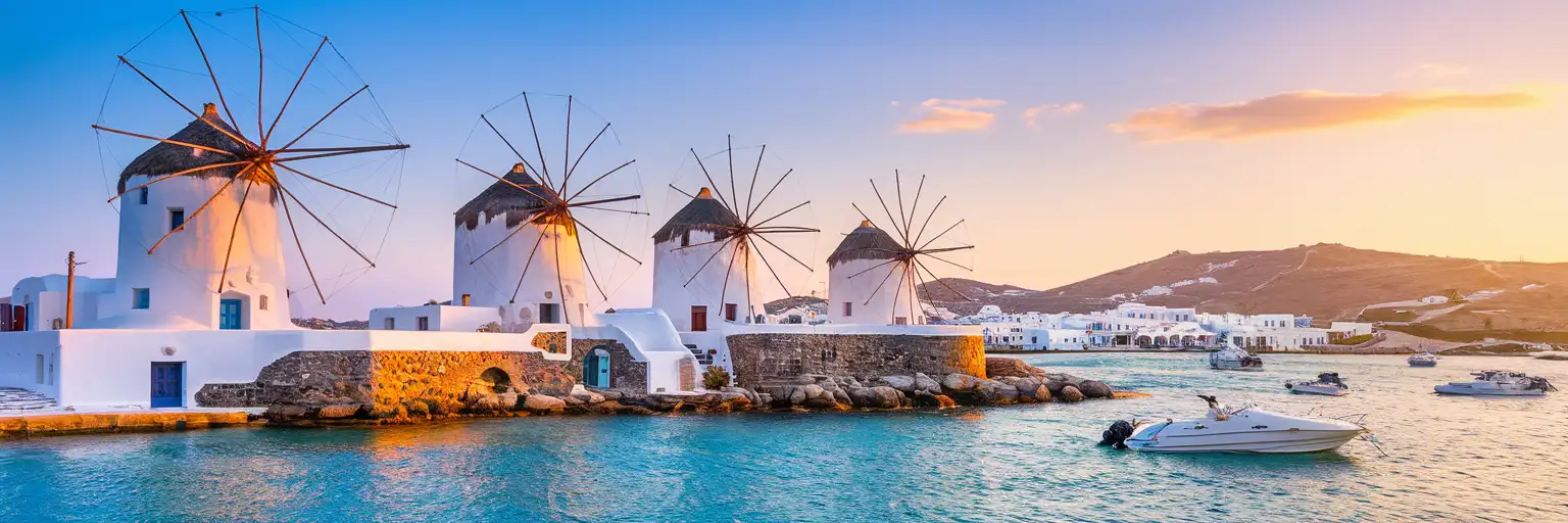 The iconic Windmills of Kato Mili in Mykonos at golden hour with the Aegean Sea and harbor in the background
