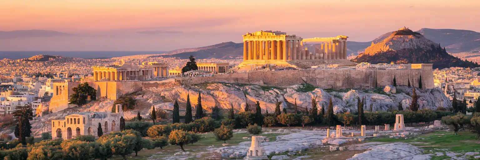 The Acropolis of Athens with the Parthenon temple at golden hour, the city of Athens spreading below toward the Aegean Sea
