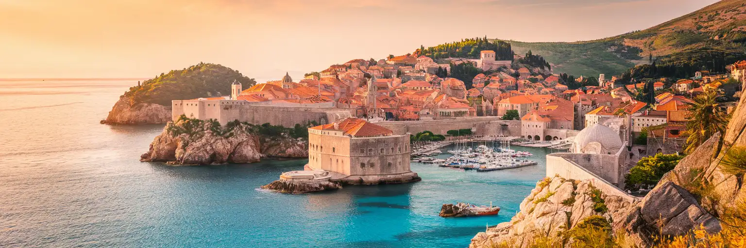 Panoramic view of Dubrovnik's medieval walled city and terracotta rooftops along the Adriatic coastline at golden hour