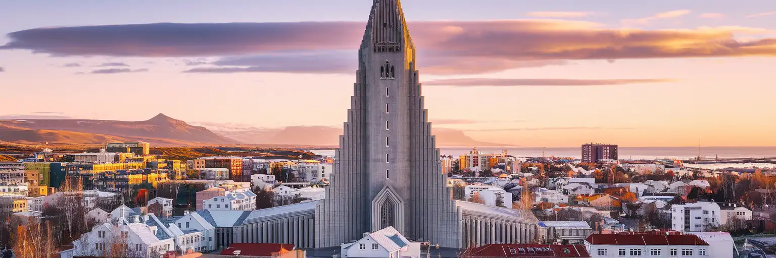 Hallgrímskirkja church towering over Reykjavík's colorful rooftops with distant mountains and North Atlantic glimpses at golden hour