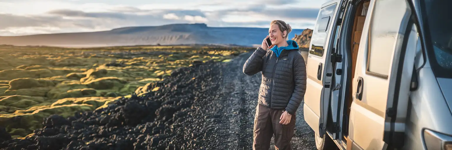 Traveler making a phone call beside a campervan on a remote Icelandic road with volcanic landscape in the background