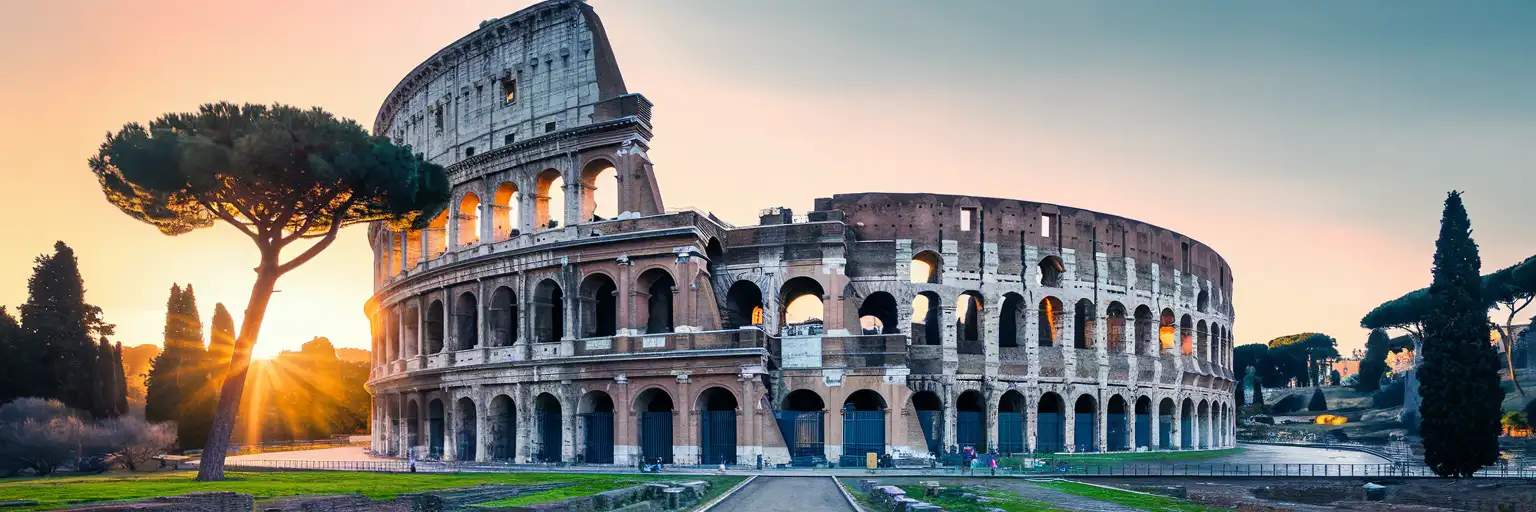 The Colosseum in Rome bathed in golden sunset light with umbrella pines framing the ancient amphitheatre