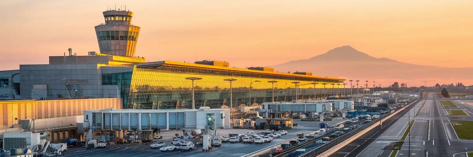 Naples International Airport Terminal 1 facade at golden hour with control tower and Mount Vesuvius in the distance