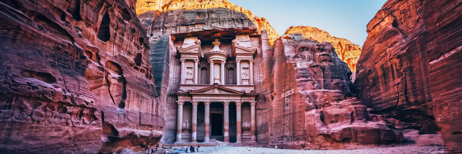The ancient Treasury of Petra carved into red sandstone cliffs viewed through the Siq canyon at golden hour in Jordan
