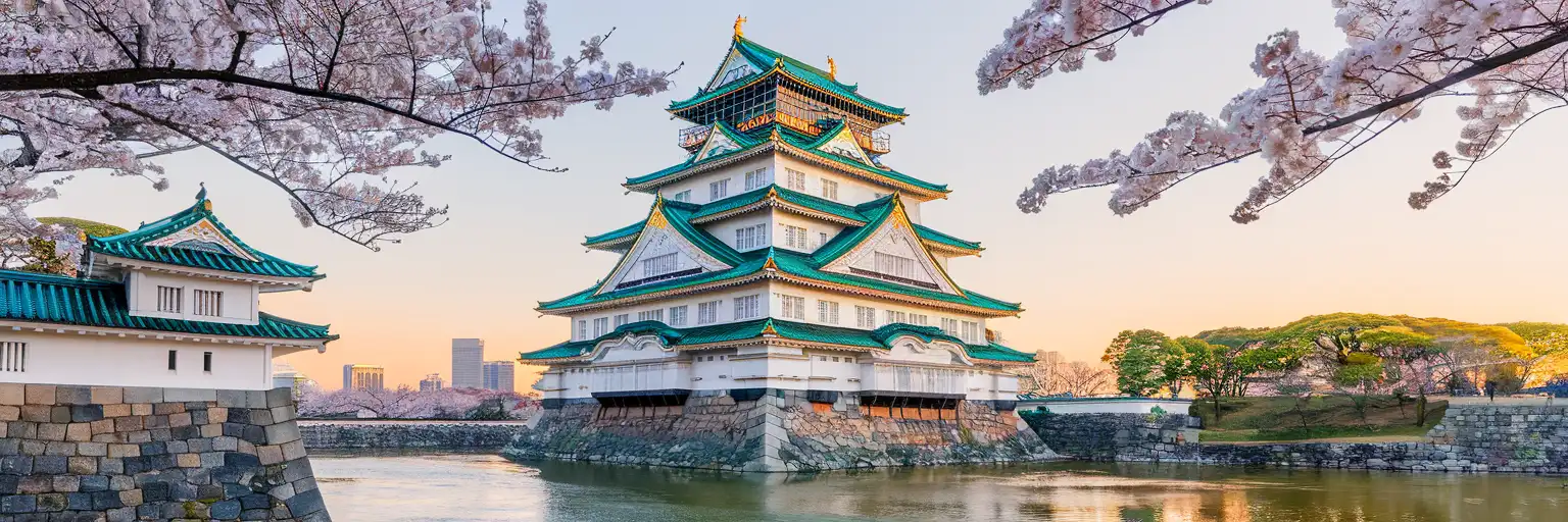 Osaka Castle main keep rising above massive stone walls at golden hour with cherry trees in foreground