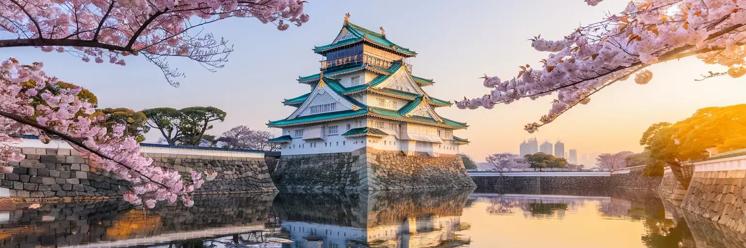 Osaka Castle at golden hour with cherry blossoms framing the white fortress walls and modern skyline in the distance