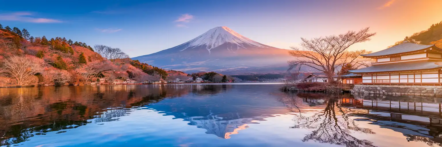 Mount Fuji with snow-capped peak reflected in a calm lake at golden hour, surrounded by Japanese forest and traditional shoreline architecture