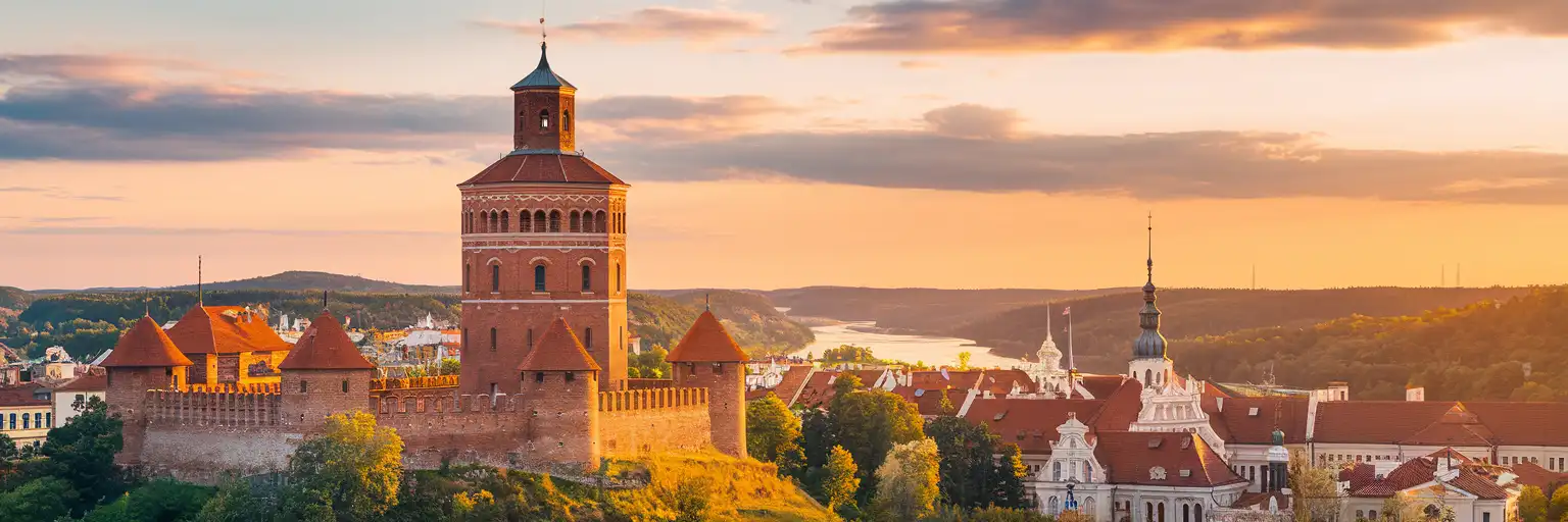 Gediminas Tower rising above Vilnius Old Town at golden hour with the Neris River valley and historic church spires in the distance