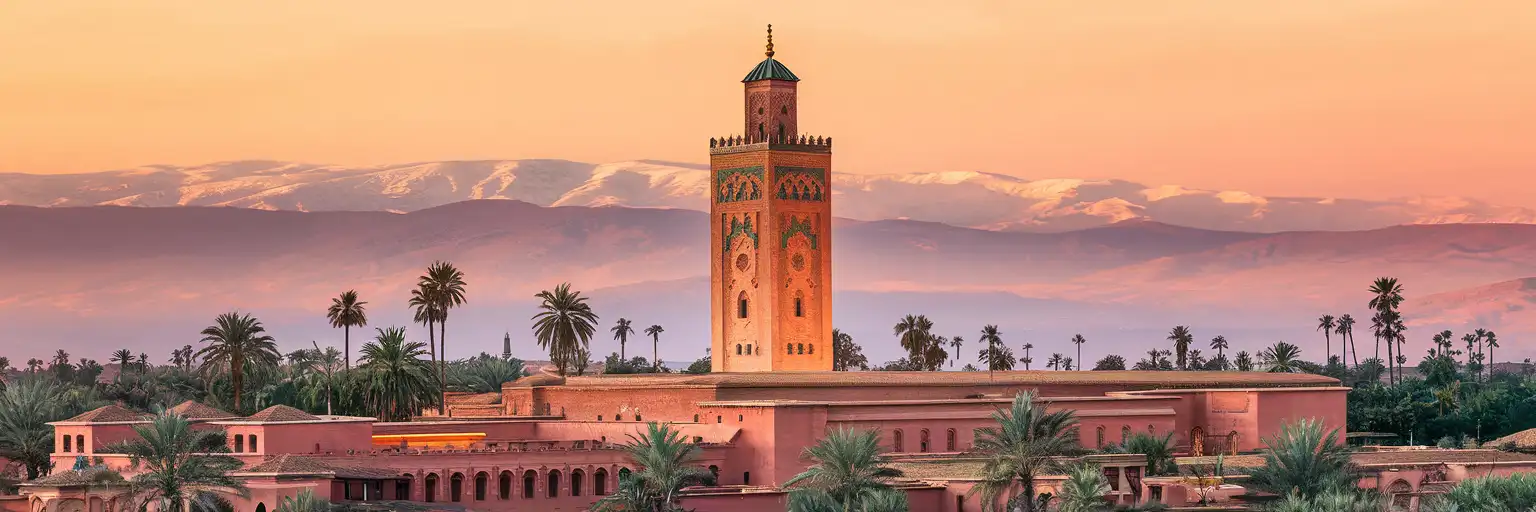 Koutoubia Mosque minaret rising above the red-ochre medina of Marrakech with Atlas Mountains in the distance at golden hour