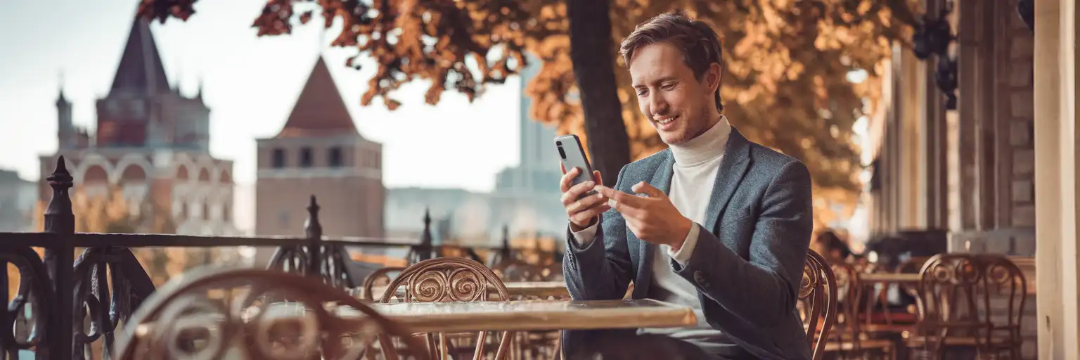 Viajero revisando una notificación de SMS en su teléfono en un café al aire libre en Chișinău, Moldavia, con calles arboladas y arquitectura local de fondo