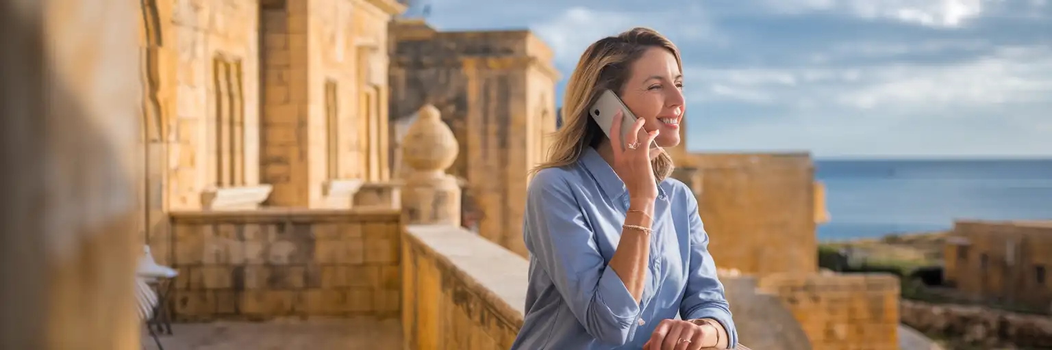Woman making a phone call on a traditional Maltese limestone balcony with Mediterranean Sea views