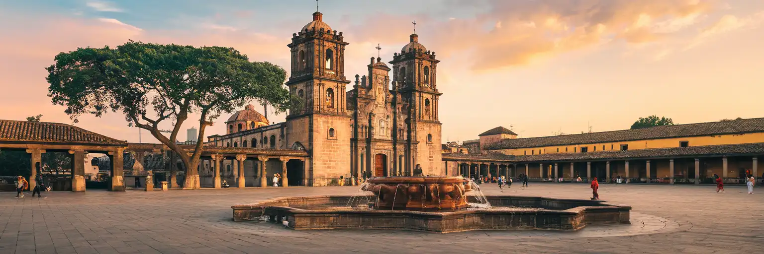 Golden-hour exterior view of Parroquia San Juan Bautista and Jardín Centenario in Coyoacán, Mexico City, Mexico