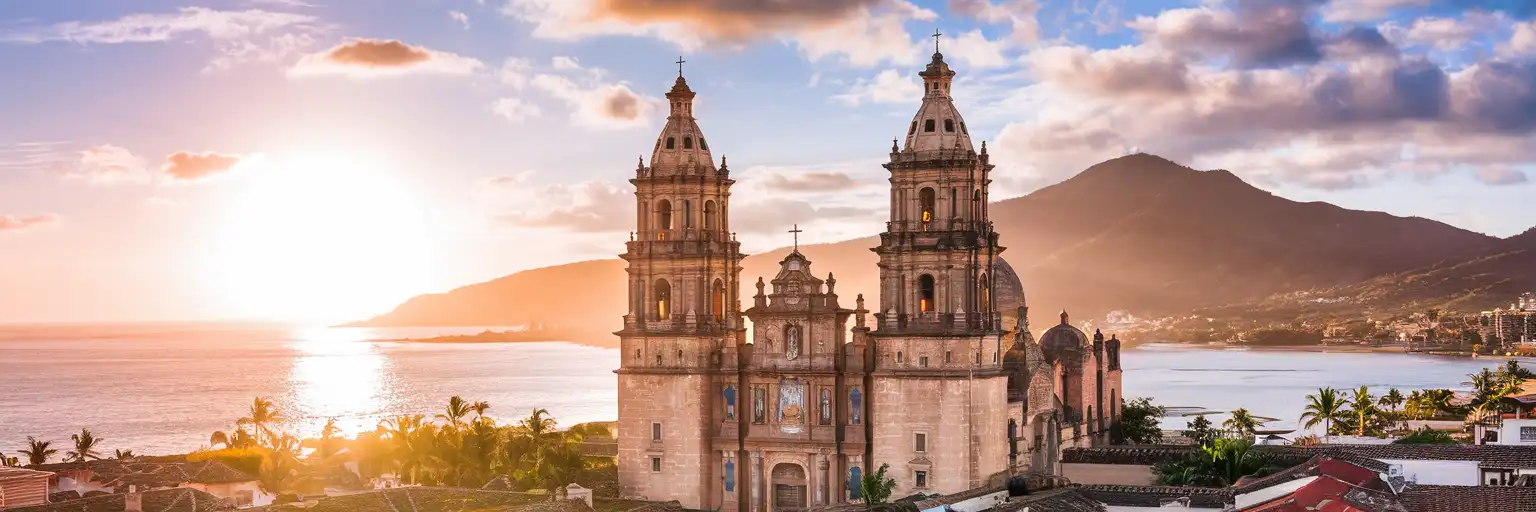 Church of Our Lady of Guadalupe rising above Puerto Vallarta's terracotta rooftops with Banderas Bay and Sierra Madre mountains at golden hour