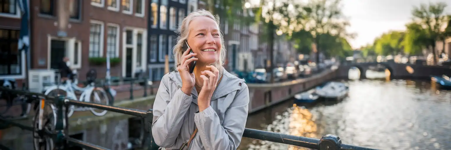 Amsterdam kanalı yanında, arka planda Hollanda tuğla binaları ile telefon görüşmesi yapan kadın gezgin