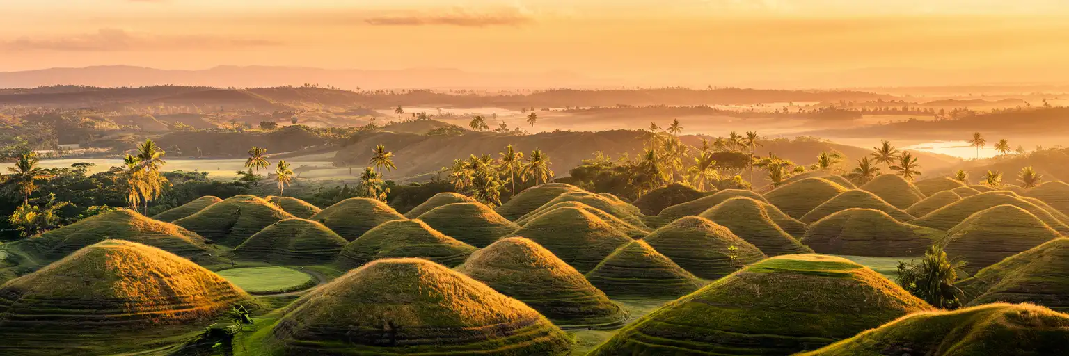 The Chocolate Hills of Bohol stretching across the Philippine landscape at golden hour with palm trees in the valleys